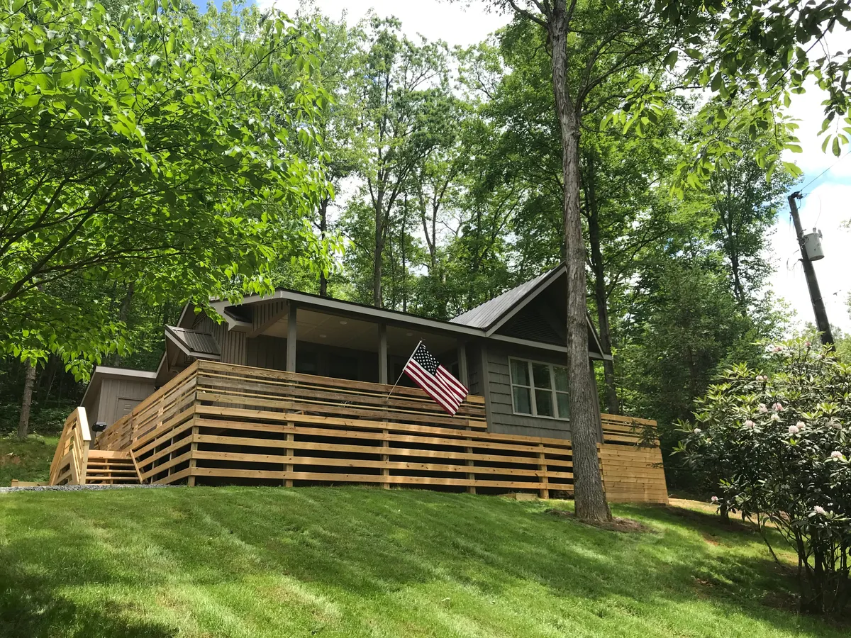 This exterior image shows the house with a spacious wooden deck, surrounded by lush greenery and flying an American flag. The deck is ready for gatherings, relaxation, or simply enjoying the scenic mountain environment.