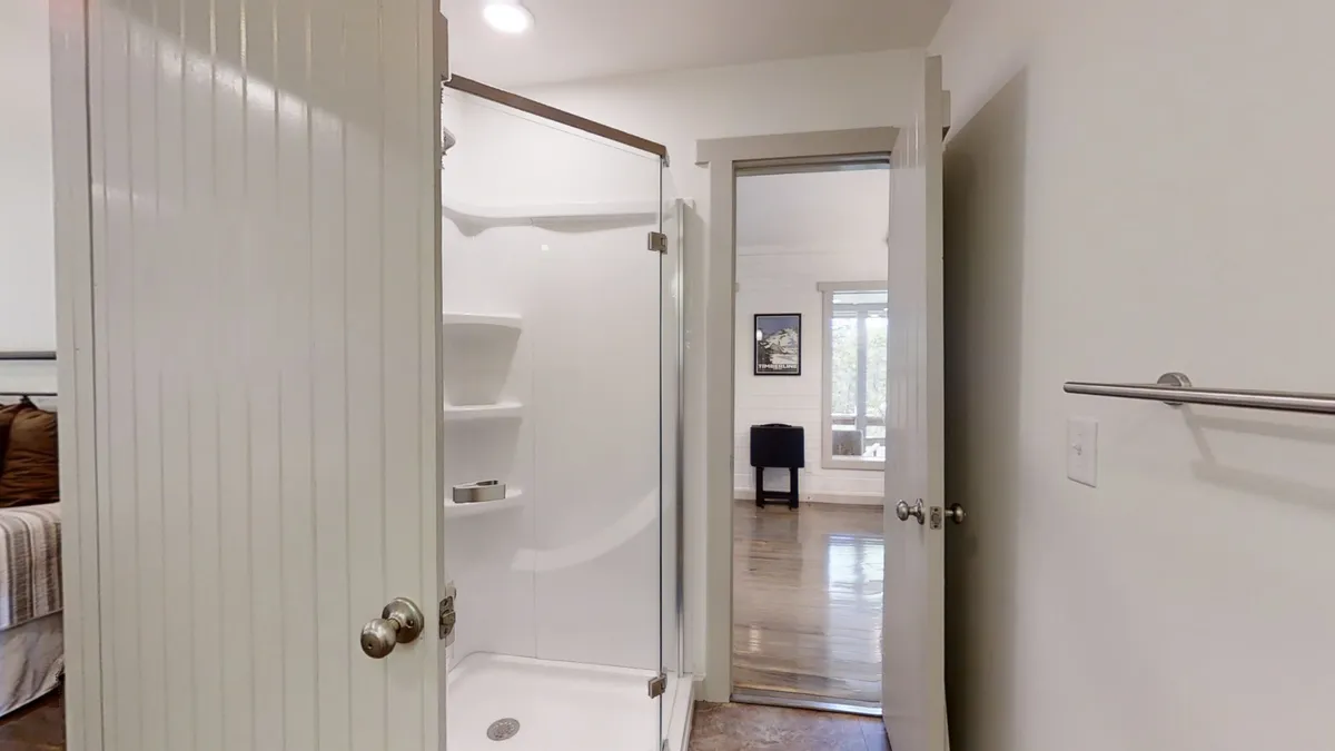A stylish interior showing a glass shower enclosure in the corner, a bed with decorative pillows, and a cozy chair. The space feels functional yet inviting, with a visible transition between the bedroom and bathroom, highlighting the seamless access and spa-like features.