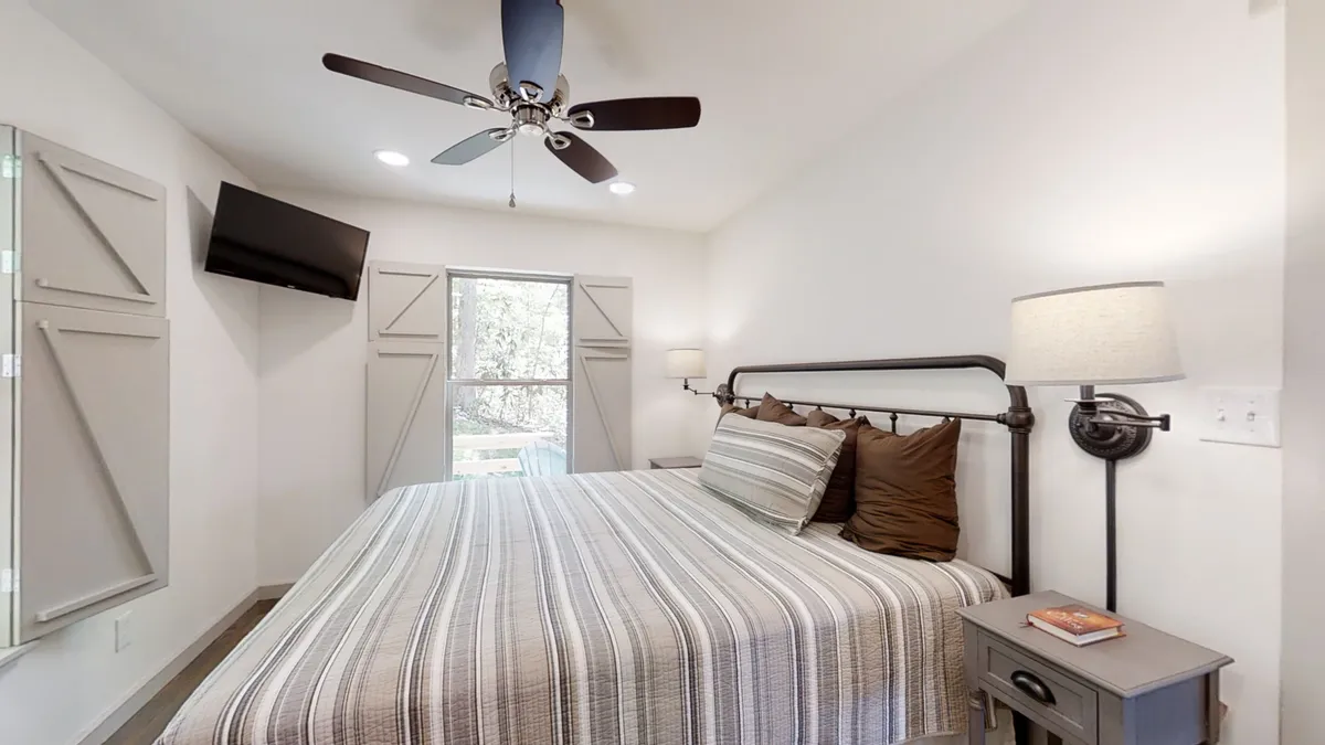 A cozy bedroom with sunlight streaming through the window, a bed inviting rest, and a nightstand for morning coffee or a good book. The window frames a view outside, inviting guests to imagine the excitement awaiting beyond the cabin.