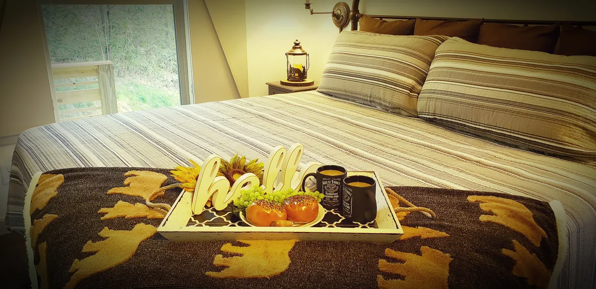 A bright, inviting king bedroom with a bed dressed in striped bedding, a decorative tray with breakfast items, and a cozy wrapped blanket. The windows are framed by custom shutters that open to natural views, creating a welcoming and restful atmosphere.