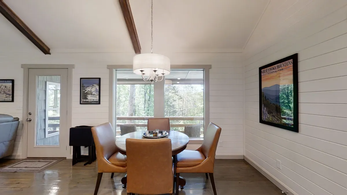 A dining area featuring large windows that frame picturesque views of the natural landscape outside. The space is bright and filled with natural light, with decorative touches and a chandelier adding warmth. Wildlife can often be seen from this vantage, reinforcing the cottage’s proximity to nature.
