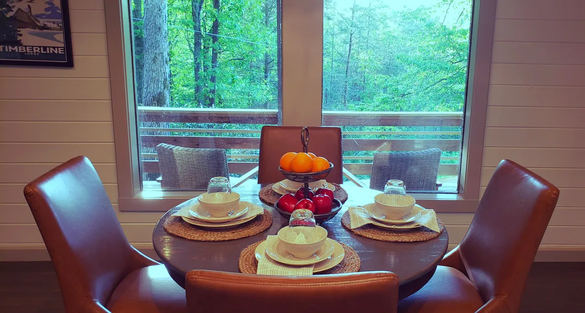 This image features a warm and welcoming dining table set near a window, with a fruit basket as its centerpiece and a view of the outdoors just beyond the glass. Natural light streams in, subtly connecting the interior space with the nature outside.