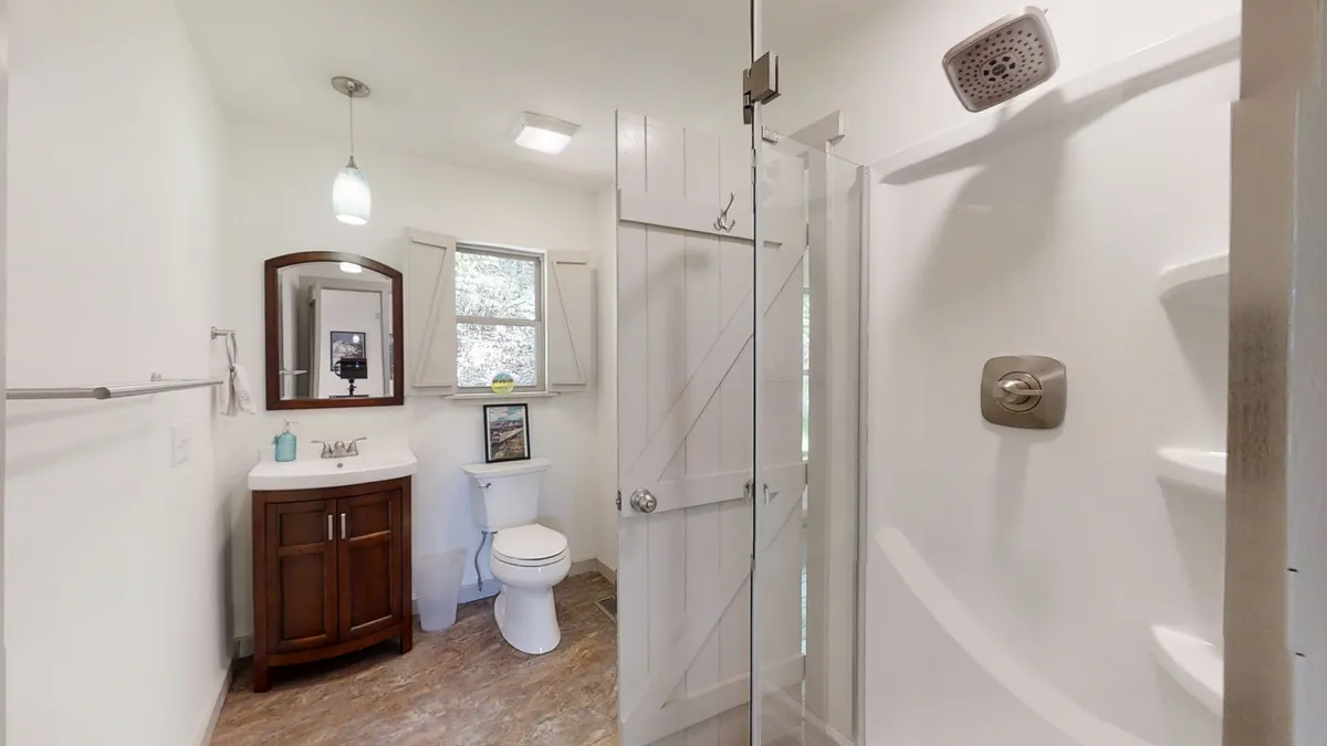 An inviting bathroom scene featuring a modern vanity with a sink, a glass shower enclosure, a well-lit mirror, and a window allowing natural sunlight to stream in. The space feels serene and thoughtfully appointed for relaxation and self-care.