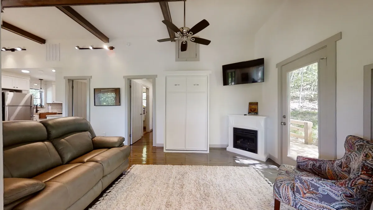 A cozy living space highlighting a leather sofa facing a flickering fireplace, a colorful armchair, a large TV, and a door leading outside. Throws are draped for extra comfort, and the setting radiates warmth and relaxation.